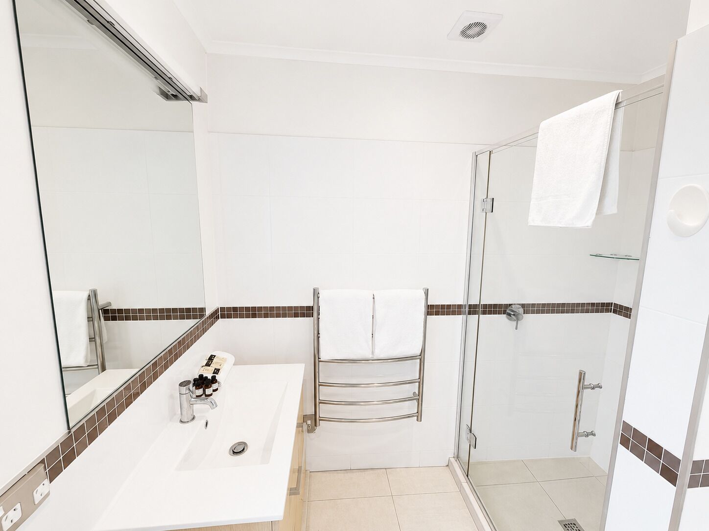 Un baño con lavamanos blanco, espejo y ducha.