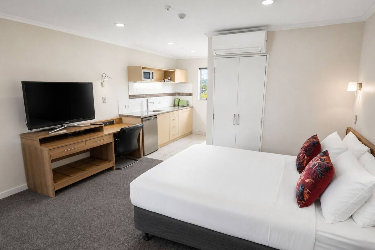 A hotel room with a bed, a TV, a desk, a kitchenette, and a wardrobe.