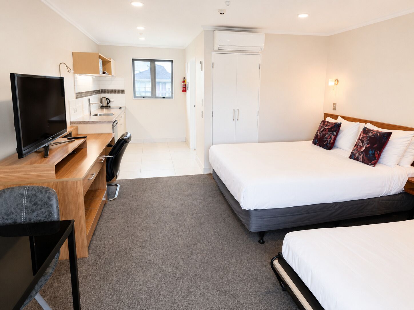A hotel room with a TV, desk, two beds, and a wardrobe.