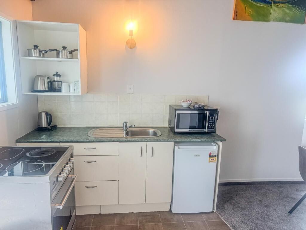 A compact kitchen with a stove, microwave, sink, and a small refrigerator.
