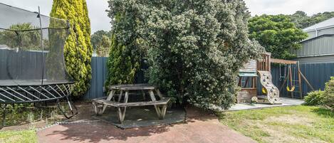 A backyard with a trampoline, picnic table, and a slide.