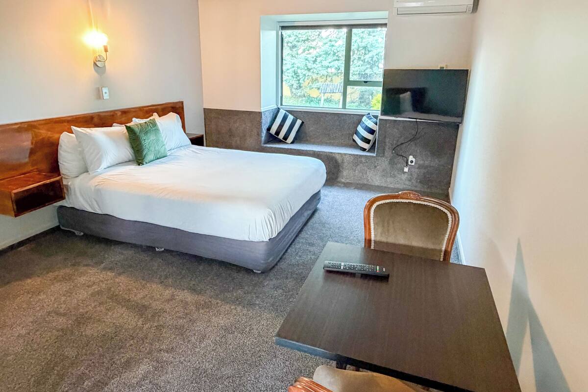 A hotel room with a bed, a TV, a small table, and a window with a view.