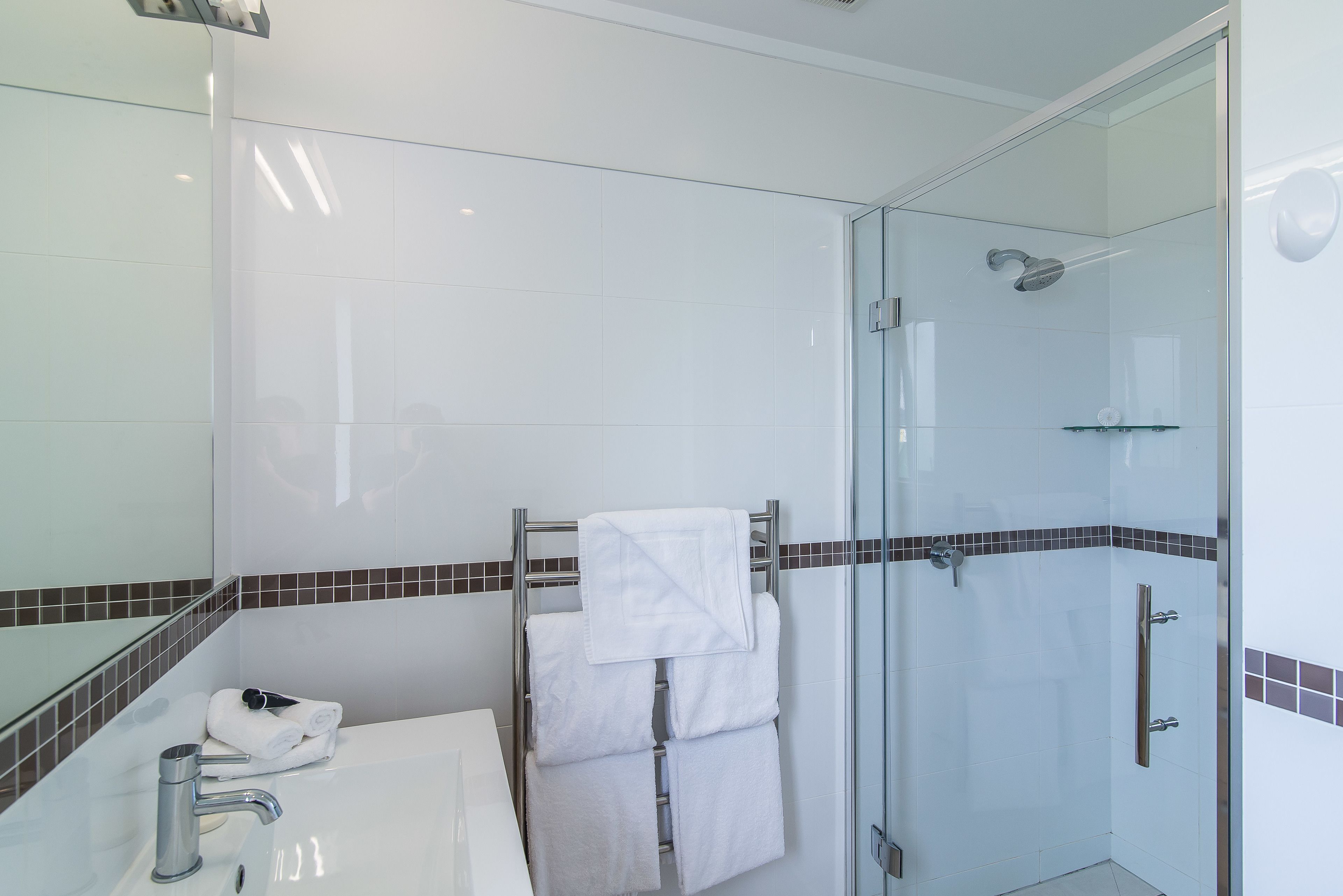 A modern bathroom with a glass-enclosed shower, a white sink, and a towel rack with neatly folded towels.