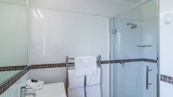 A modern bathroom with a glass-enclosed shower, a white sink, and a towel rack with neatly folded towels.