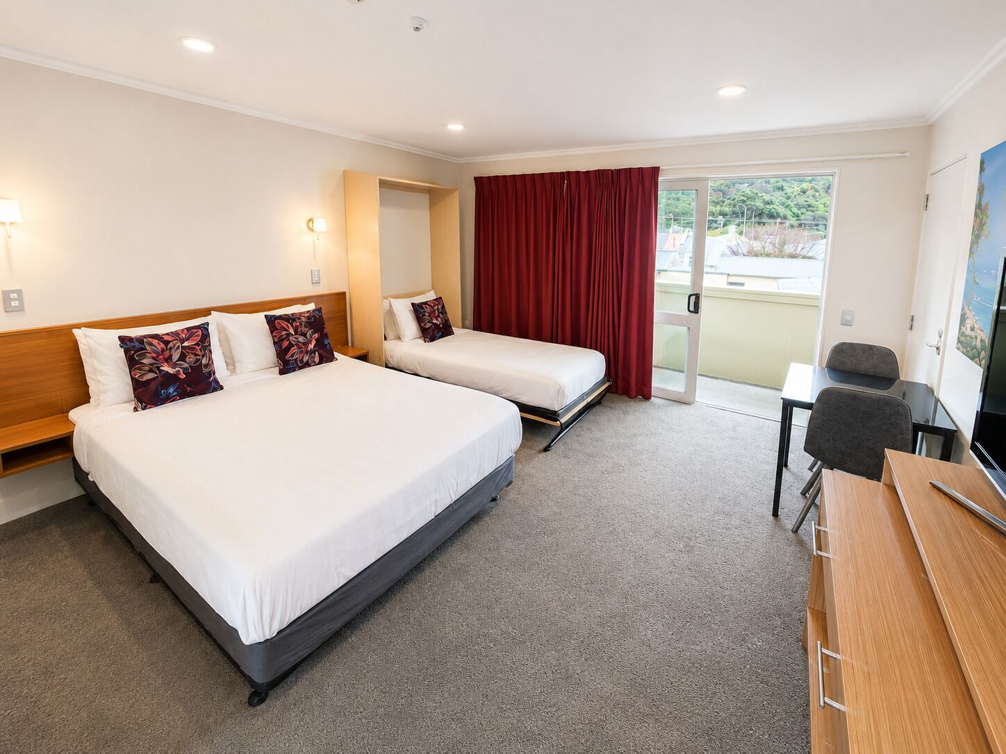A hotel room with two beds, a desk, a chair, and a television.