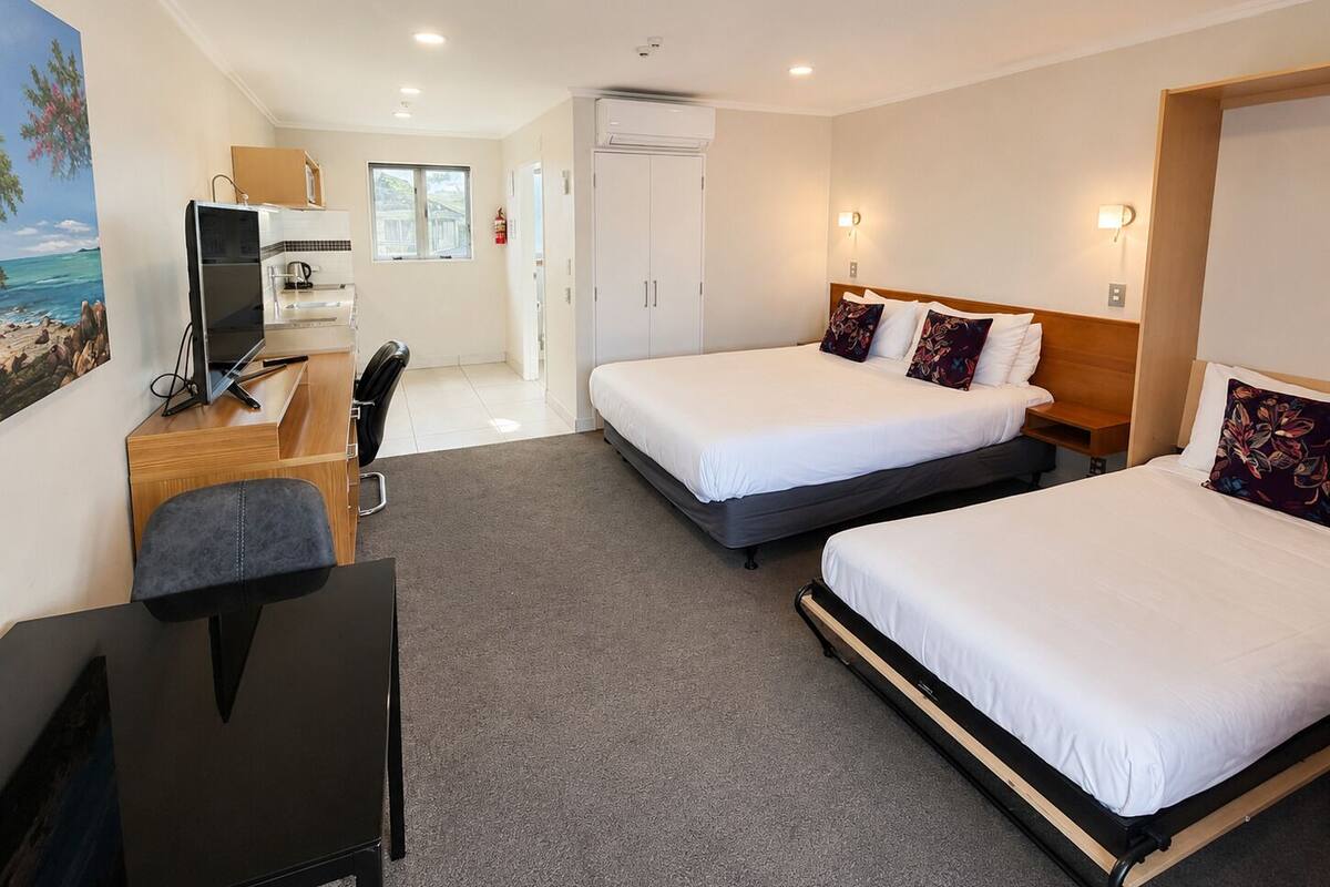 A hotel room with two beds, a desk with a computer, a chair, and a painting of a beach scene.