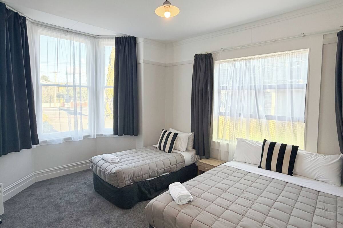 A hotel room with two beds, a ceiling light, and large windows with curtains.