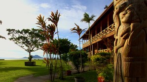 A building with a wooden facade and a balcony with a railing. There are palm trees and a pathway leading to the building. - Rapopo Plantation Resort (Kokopo)