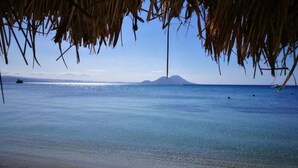 A beach with clear water, a distant mountain, and a thatched roof structure. - Rapopo Plantation Resort (Kokopo)