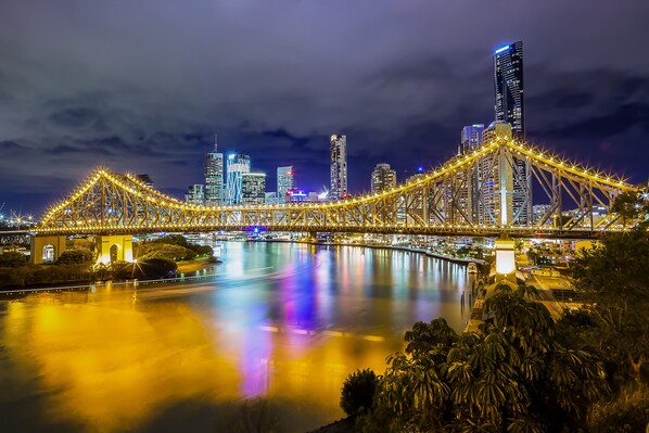 Un paisaje urbano nocturno con un puente iluminado que destaca, cruzando un cuerpo de agua que refleja las luces de la ciudad.