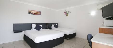 Habitación de hotel con una cama grande, una cama más pequeña, un escritorio, una silla, un televisor y un cuadro en la pared.