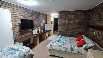 A hotel room with brick-patterned walls, a flat-screen TV, a desk with a microwave, two beds with floral bedding, and a wardrobe.