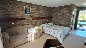 A room with a brick-patterned wall, a bed with floral bedding, a beige sofa, and a small table.