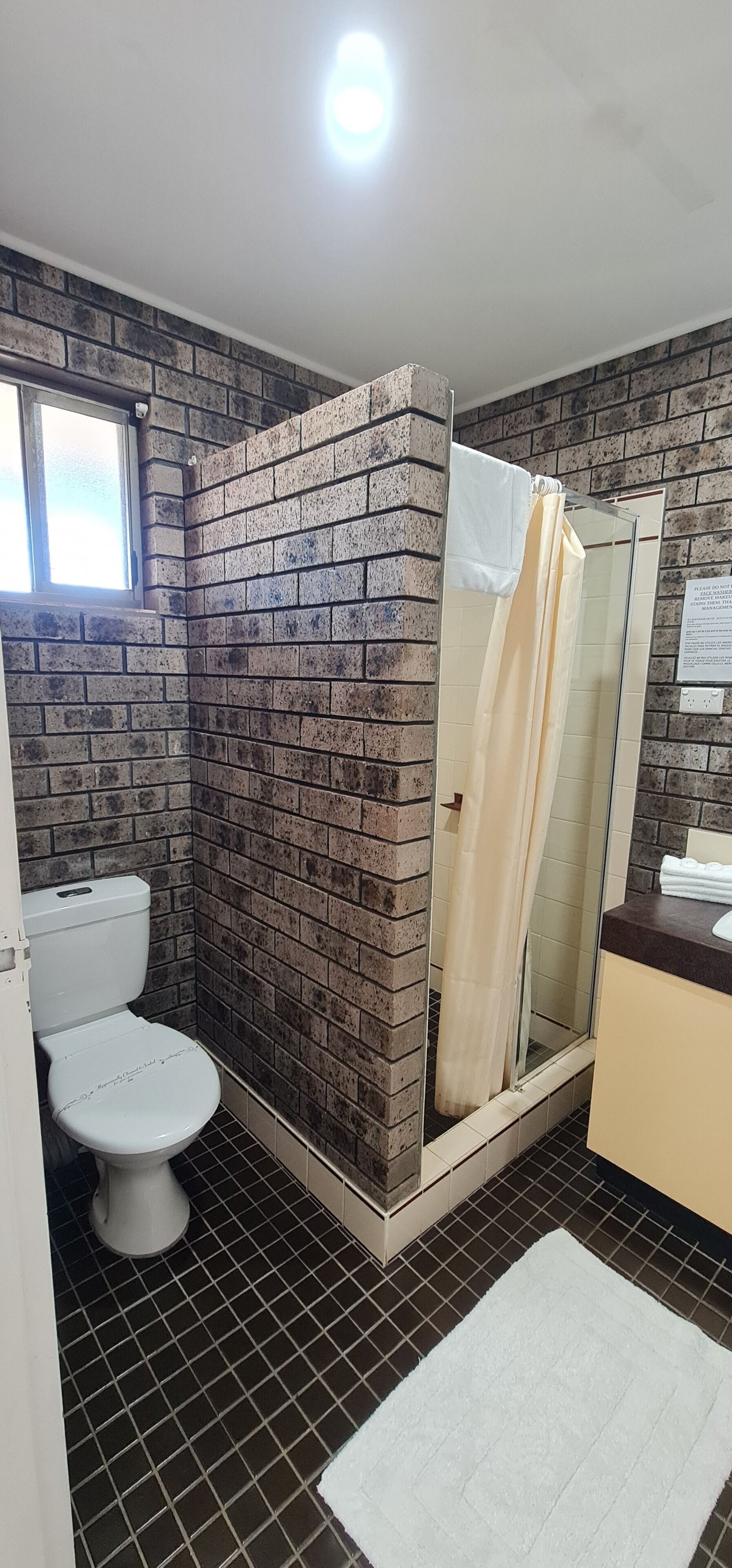 A bathroom with a toilet, a shower with a glass door, a sink, and a window.