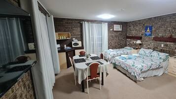 A room with a brick wall, two beds with floral bedding, a desk with a laptop, and a small table with chairs.