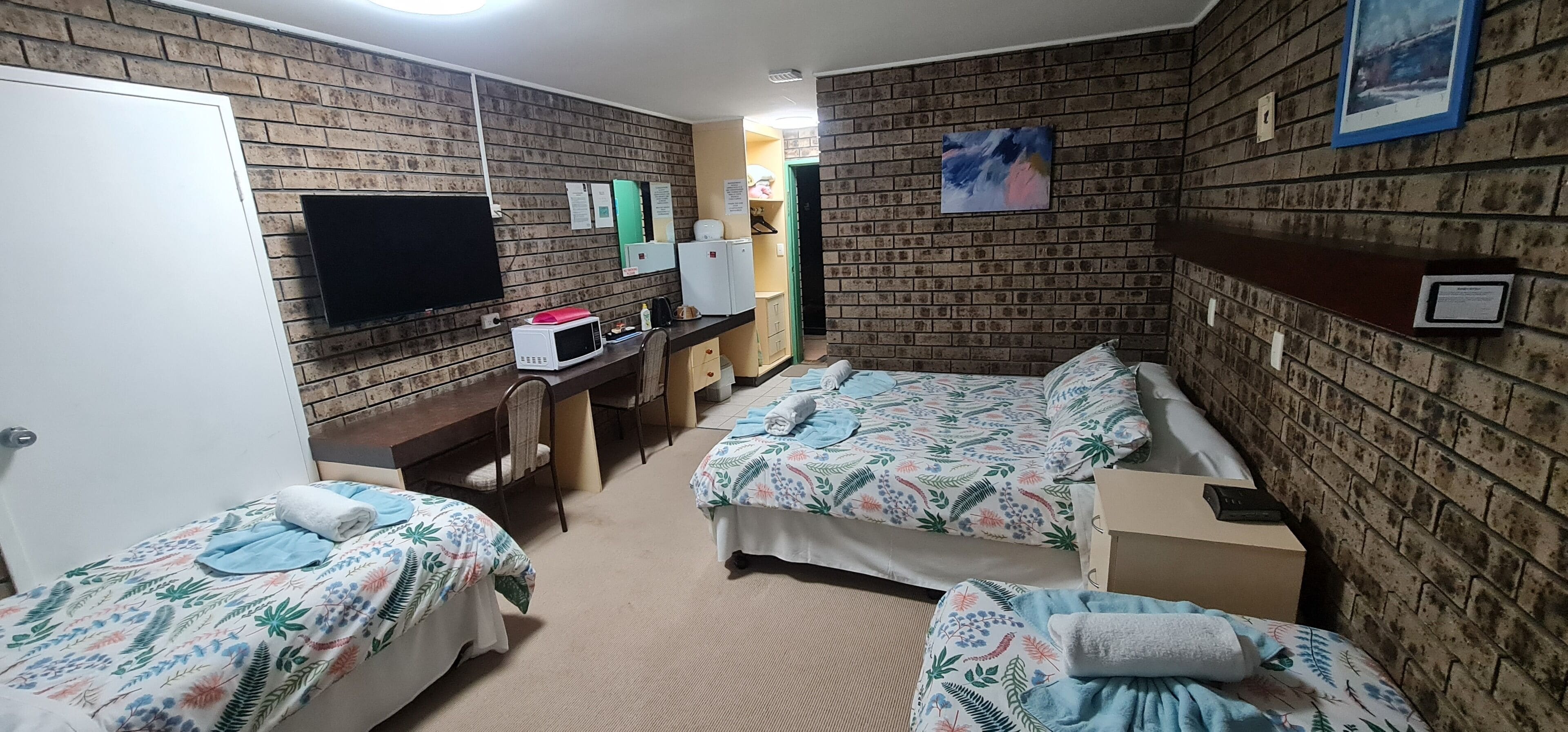 Hotelkamer met twee bedden, een bureau met een magnetron, een televisie en een wand met bakstenen patroon.