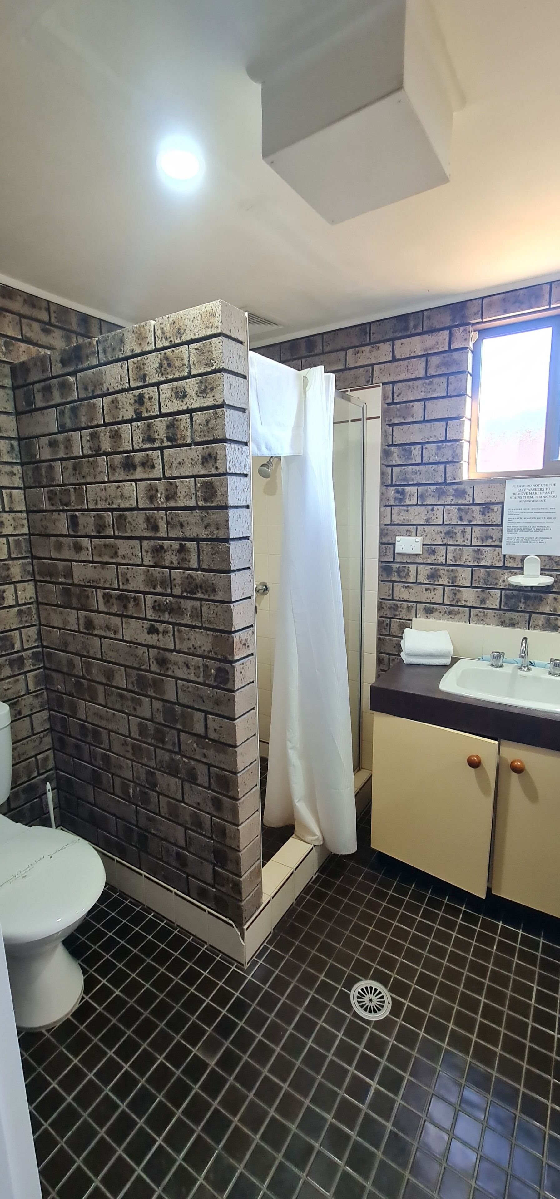 Un baño con ducha, inodoro, lavamanos y pared de ladrillo.