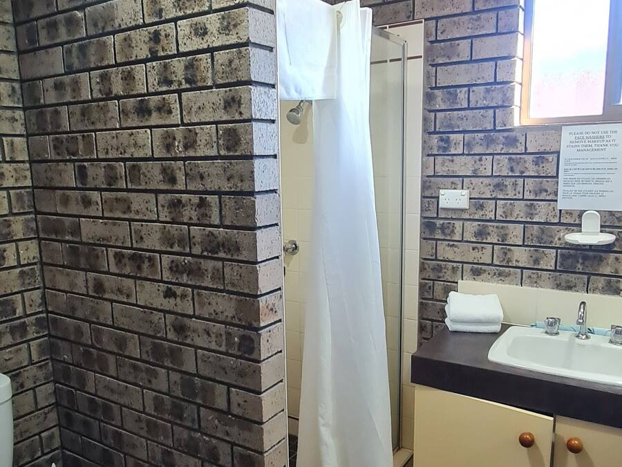 Un baño con ducha, inodoro, lavamanos y pared de ladrillo.