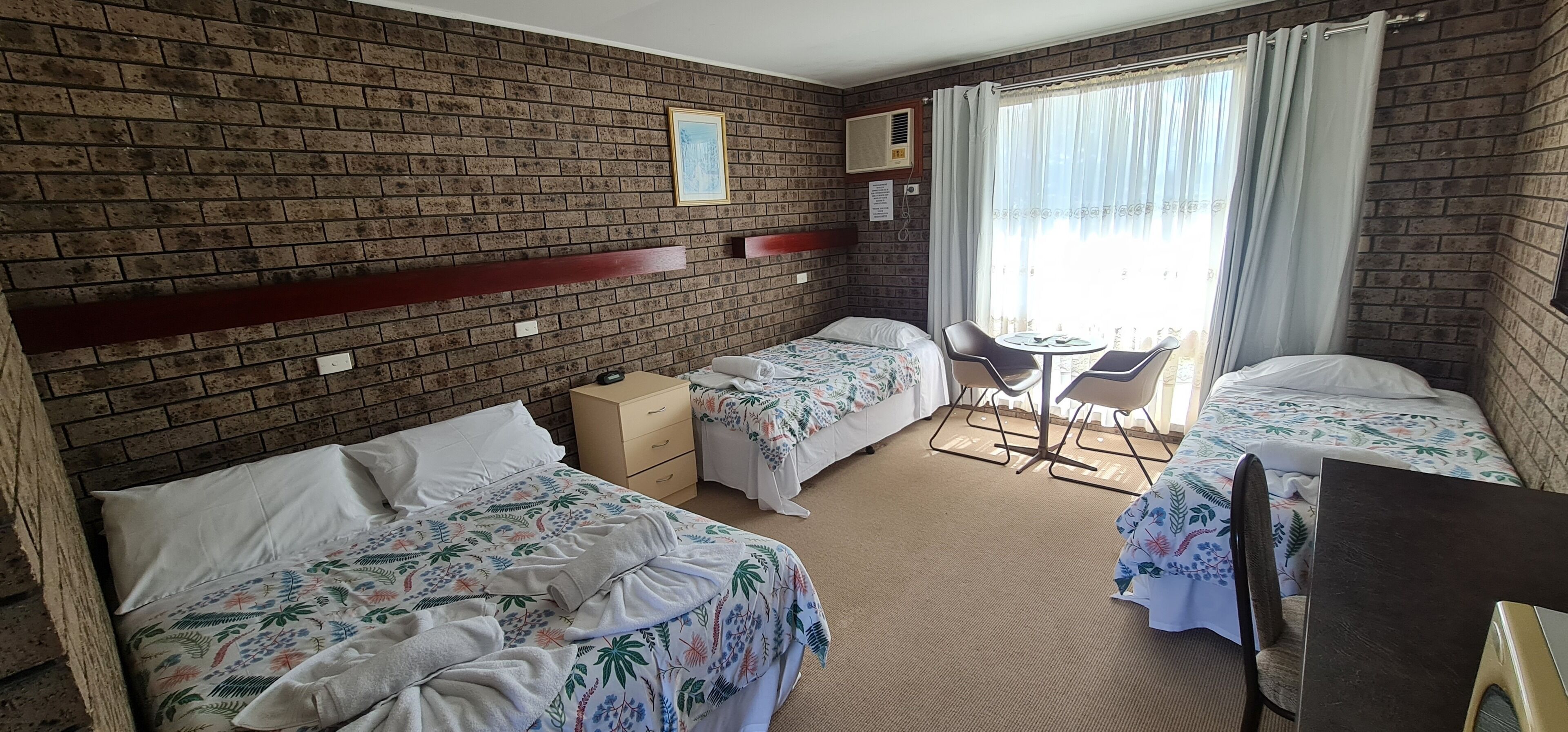 A hotel room with two single beds, a small table, and a chair.