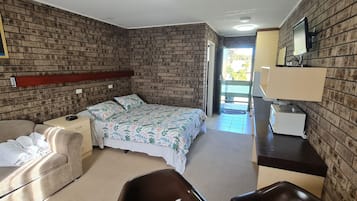 Relax in this cozy retreat with a comfortable bed, desk, and sofa, surrounded by a rustic brick wall design and a window offering a view of the outdoors.