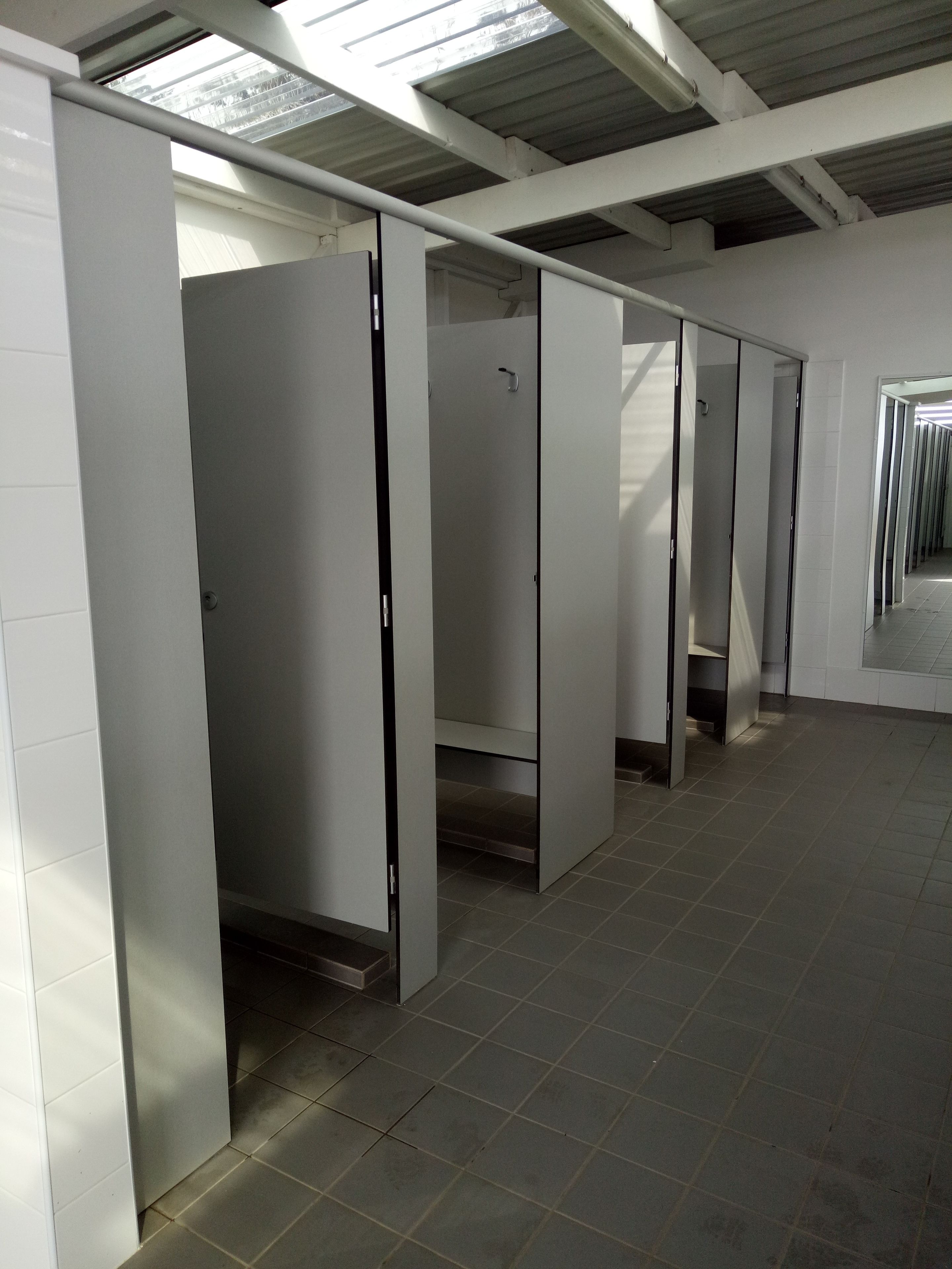 Una fila de baños separados, blancos, con suelo de baldosas y tragaluces.