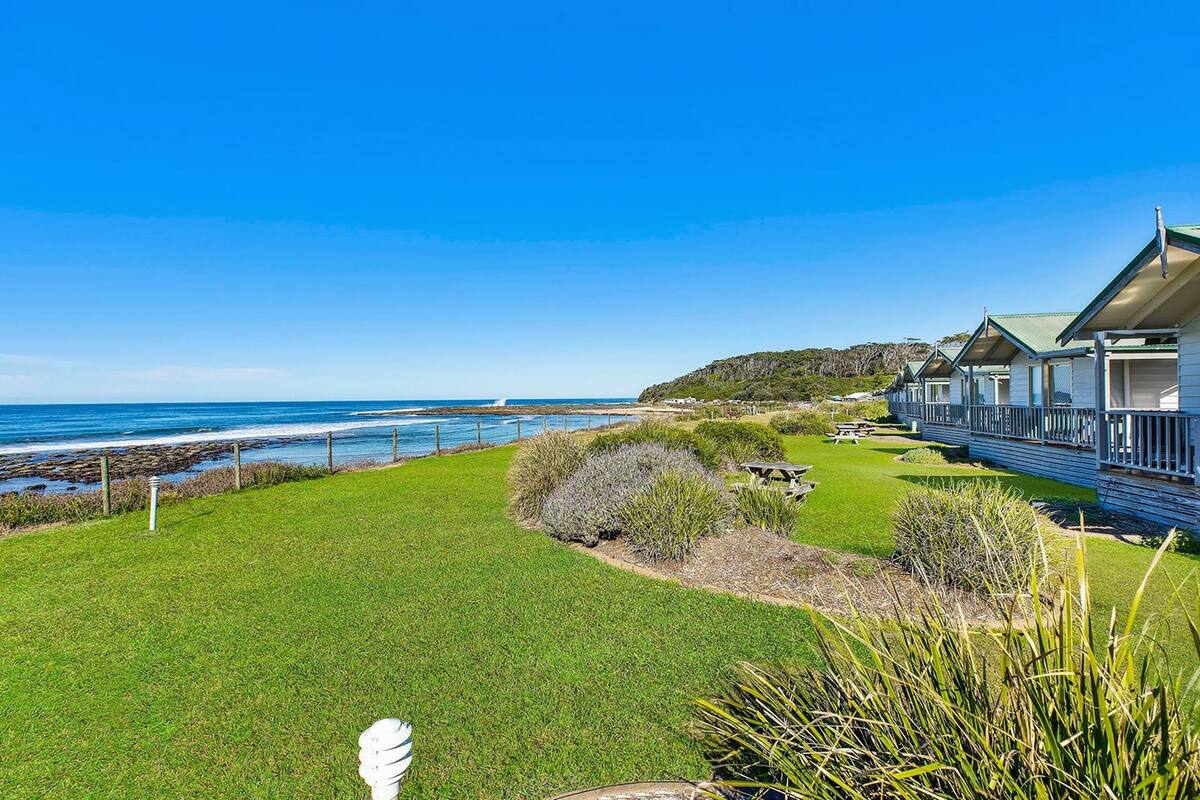 Un hôtel en bord de mer doté d’une pelouse verdoyante, d’une vue sur l’océan et de plusieurs cabanes situées au bord de la plage.