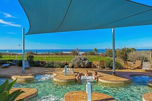Área da piscina com vista para o oceano, cercada por espreguiçadeiras e um toldo coberto.