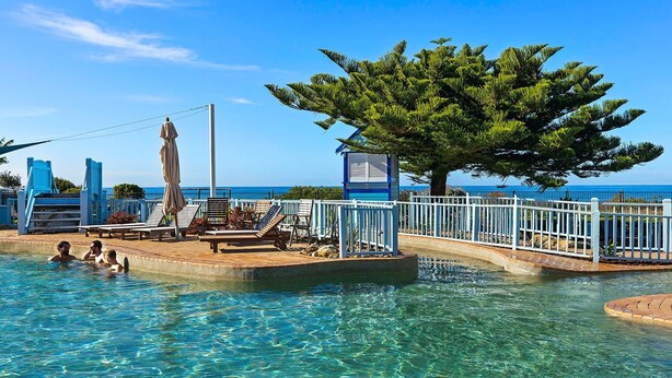 A clear swimming pool with lounge chairs and a tree. - Blue Lagoon Beach Resort (Bateau Bay)
