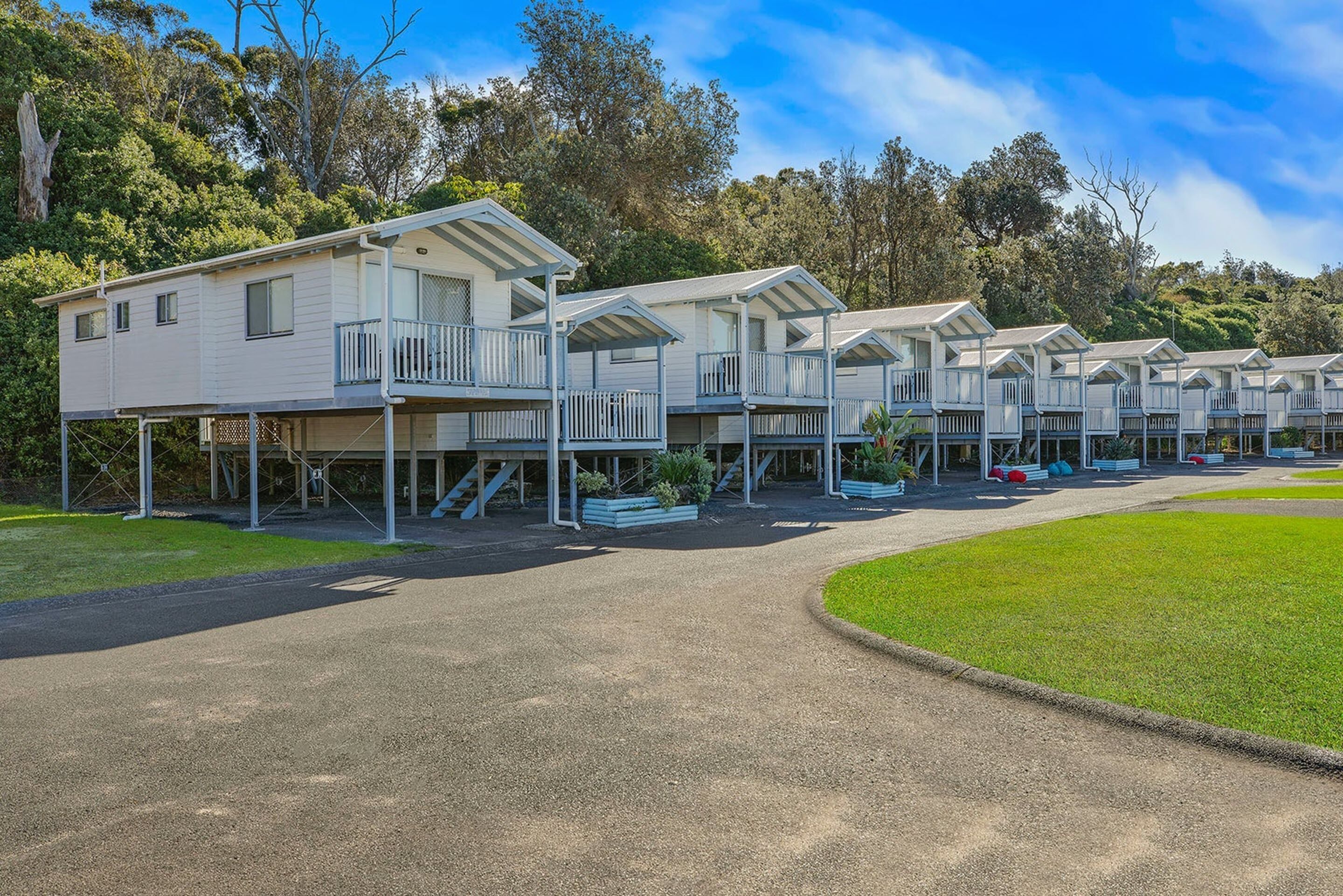 A row of white mobile homes with balconies, set in a grassy area with trees in the background.