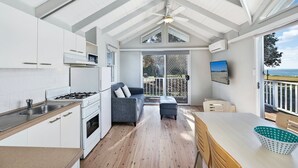 A modern kitchen with white cabinets, a gas stove, and a large window overlooking a deck. - Blue Lagoon Beach Resort (Bateau Bay)