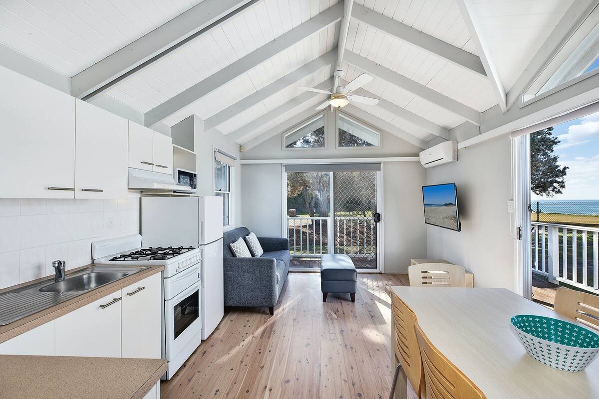 Une cuisine moderne avec des meubles blancs, une cuisinière à gaz et une grande fenêtre donnant sur une terrasse.
