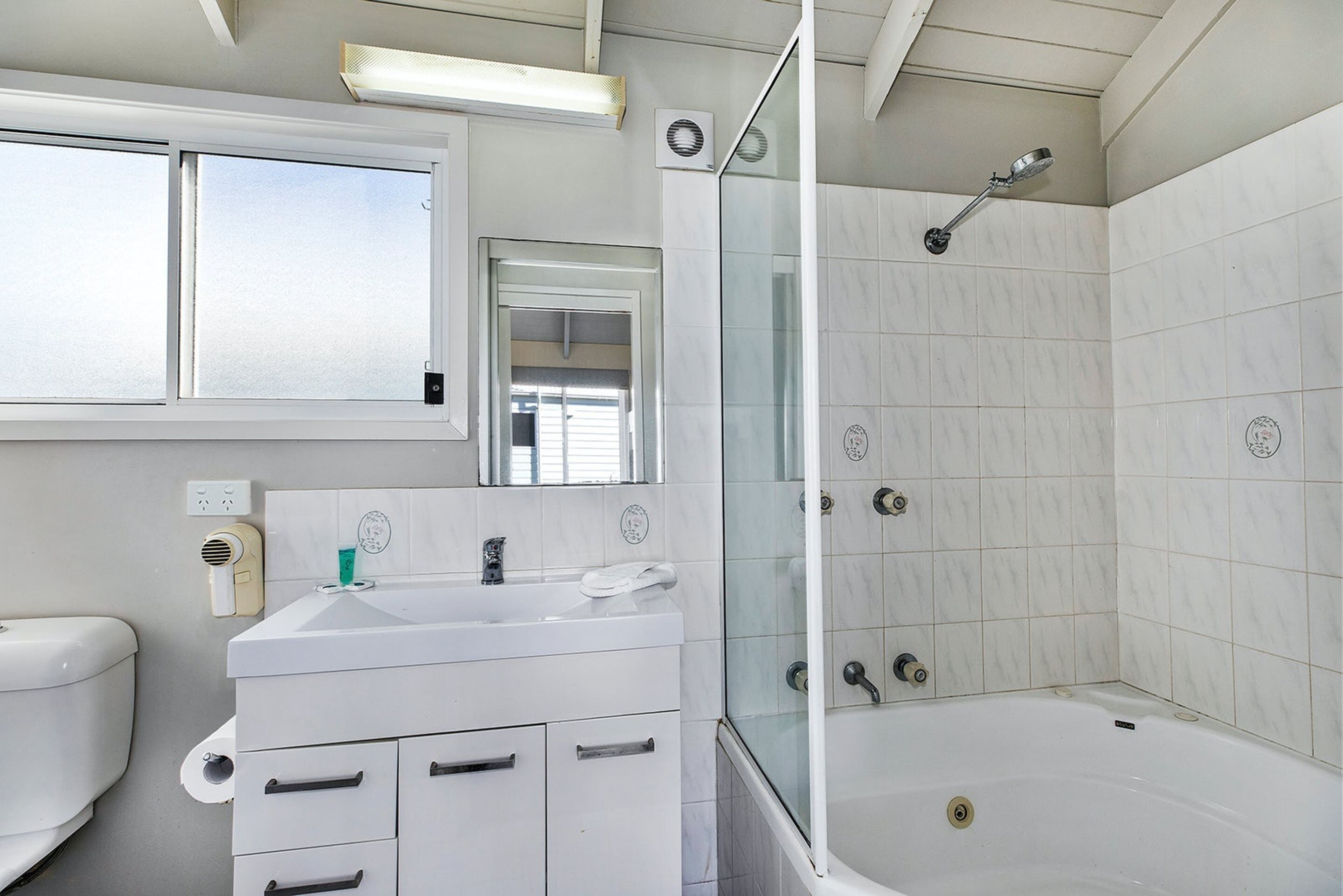 Un baño con lavamanos blanco, espejo y cabina de ducha con mampara de vidrio.