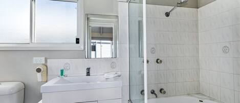 Un baño con lavamanos blanco, espejo y cabina de ducha con mampara de vidrio.
