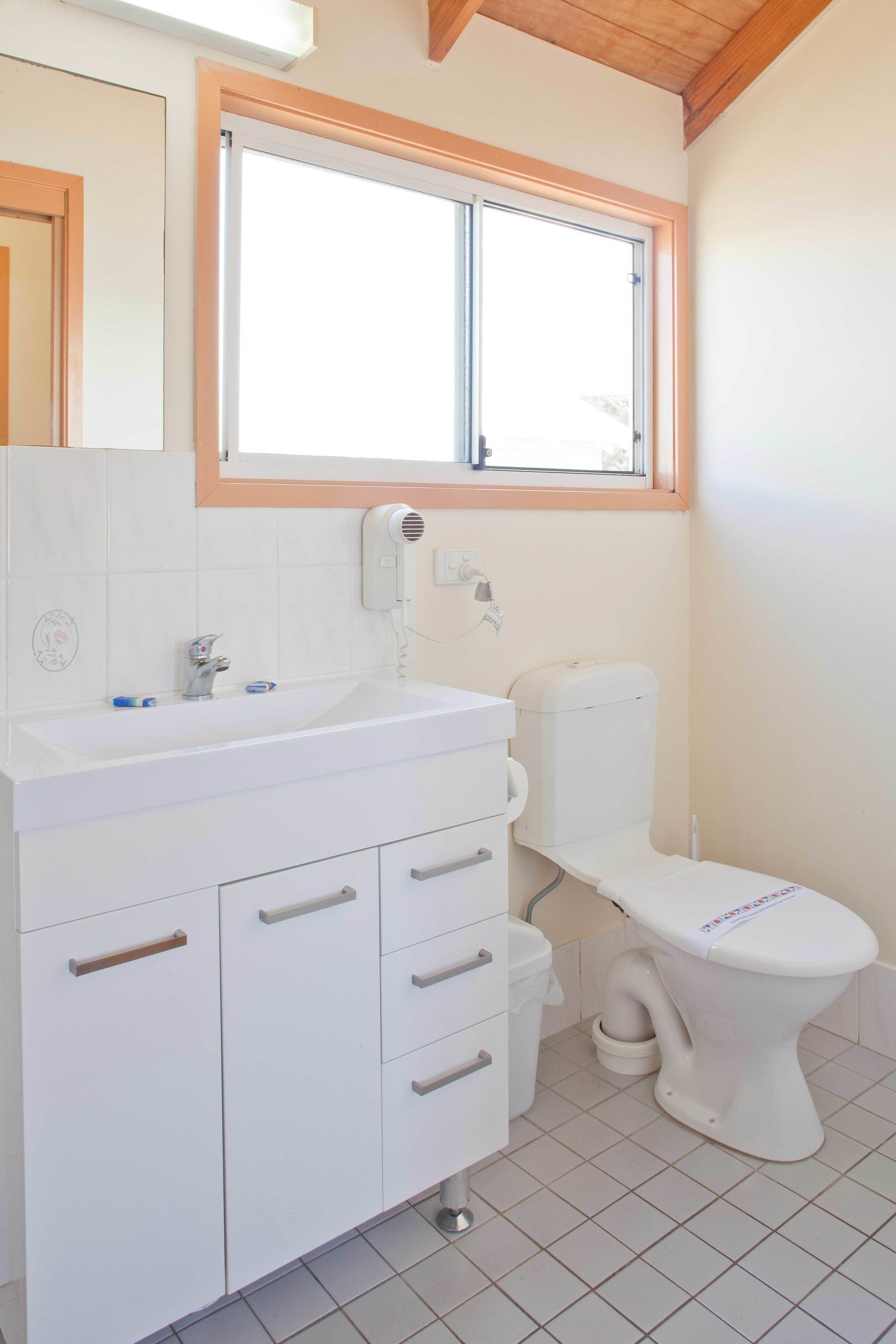 A bathroom with a white sink, vanity, and toilet. There is a window above the sink and a towel rack on the wall.