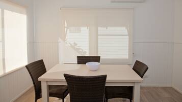 A dining area with a table, four chairs, a bowl, and a window with blinds.
