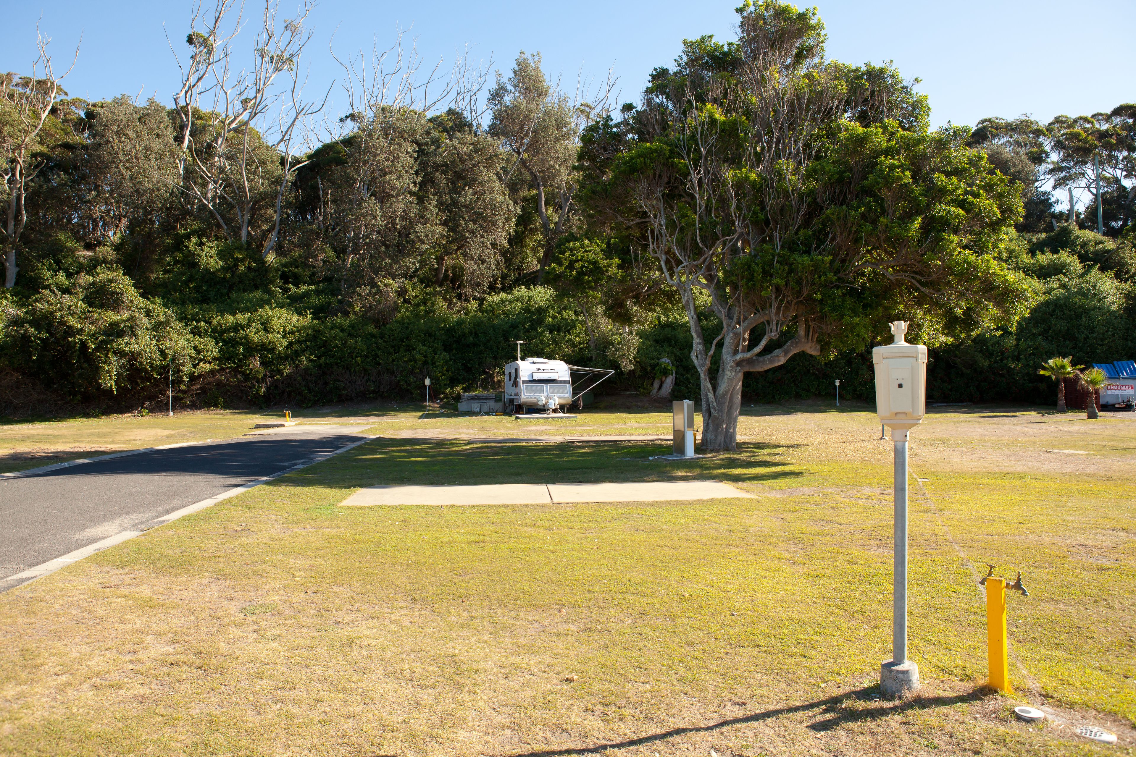 Un terrain de camping avec un camping-car blanc, des arbres et un hydrant d’incendie jaune.
