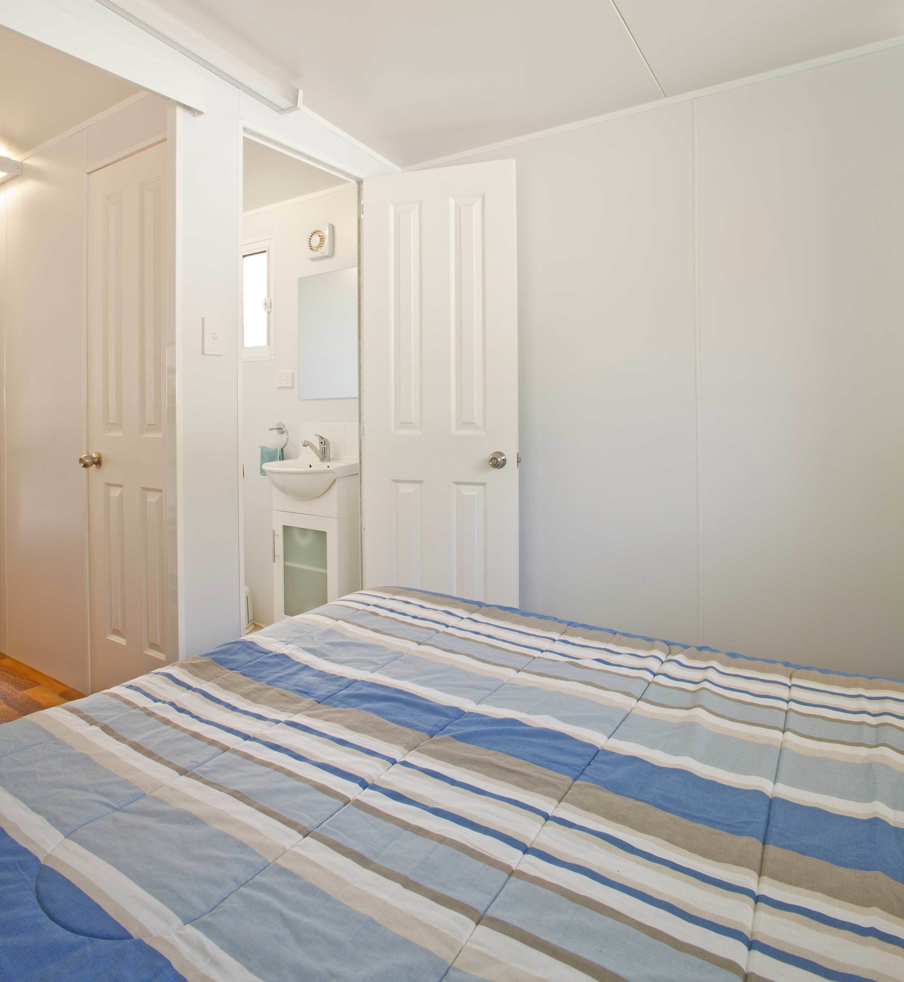 Un dormitorio con cama, puerta, baño pequeño y un interruptor de luz en la pared.