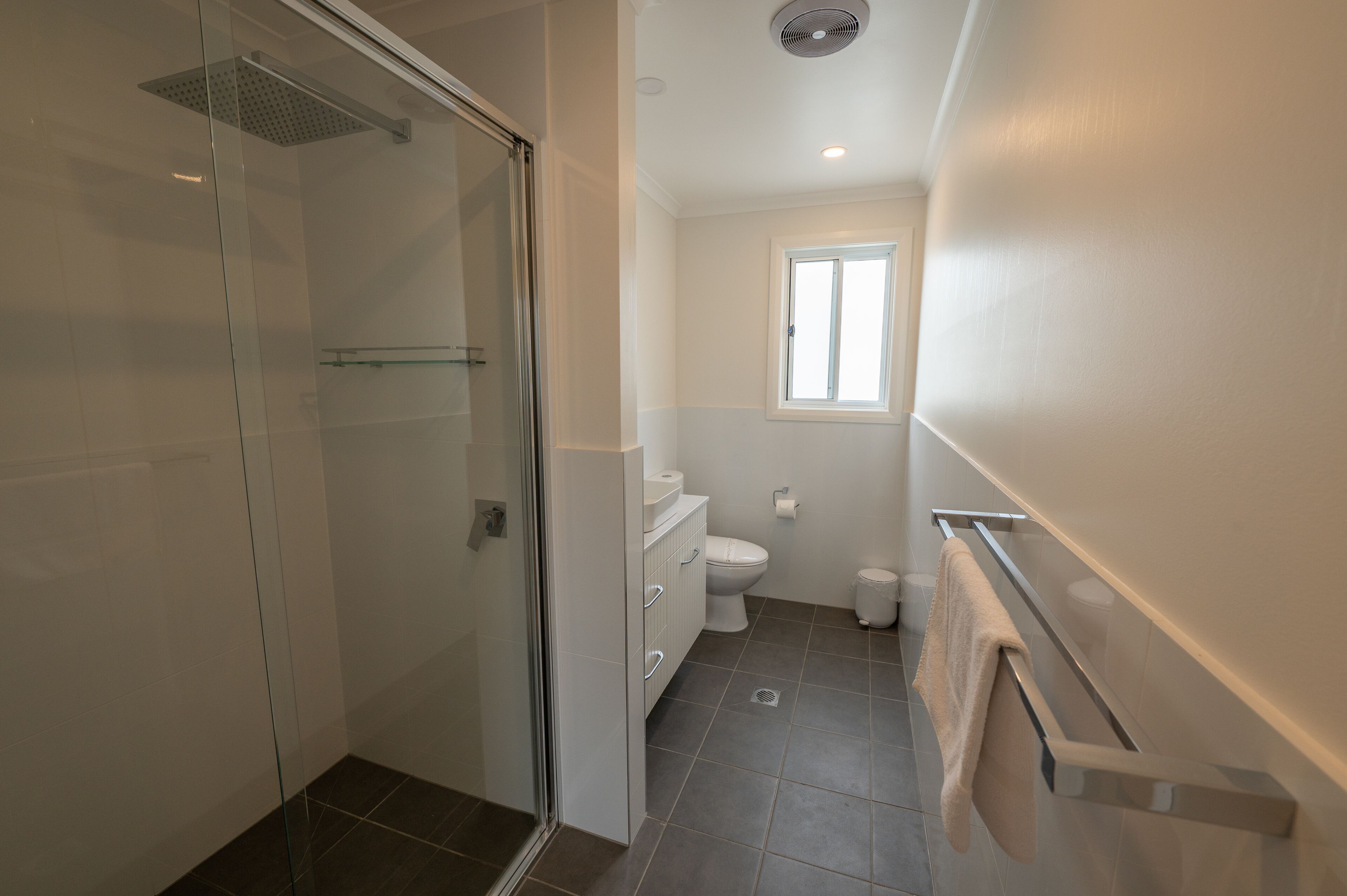 Une salle de bain avec une douche à parois de verre, des toilettes et une fenêtre.