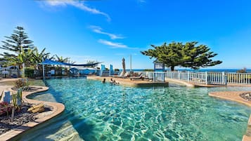 Una piscina al aire libre, sombrillas, sillones reclinables de piscina