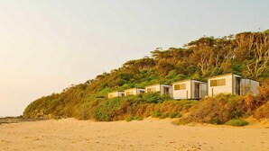 A beach with several small, single-story cabins built on a hillside. - Blue Lagoon Beach Resort (Bateau Bay)