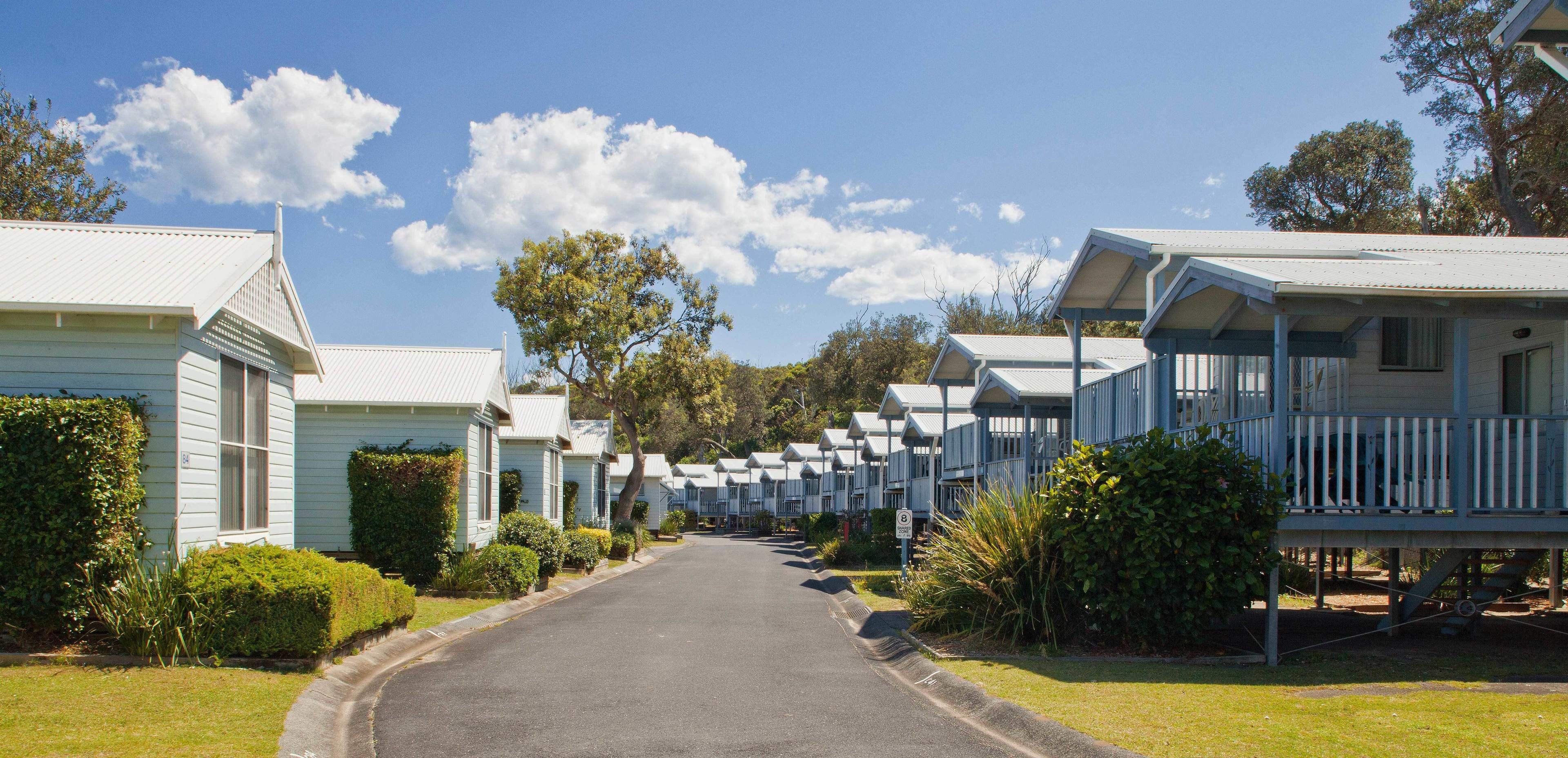 A row of light blue mobile homes with white railings, a clear sky, and a well-maintained lawn.