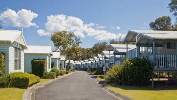 A row of light blue mobile homes with white railings, a clear sky, and a well-maintained lawn.