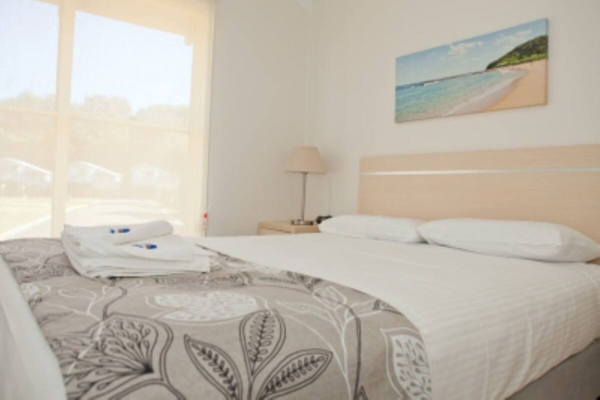 Une chambre d’hôtel avec un lit, une table de chevet, une lampe et un tableau représentant une plage.