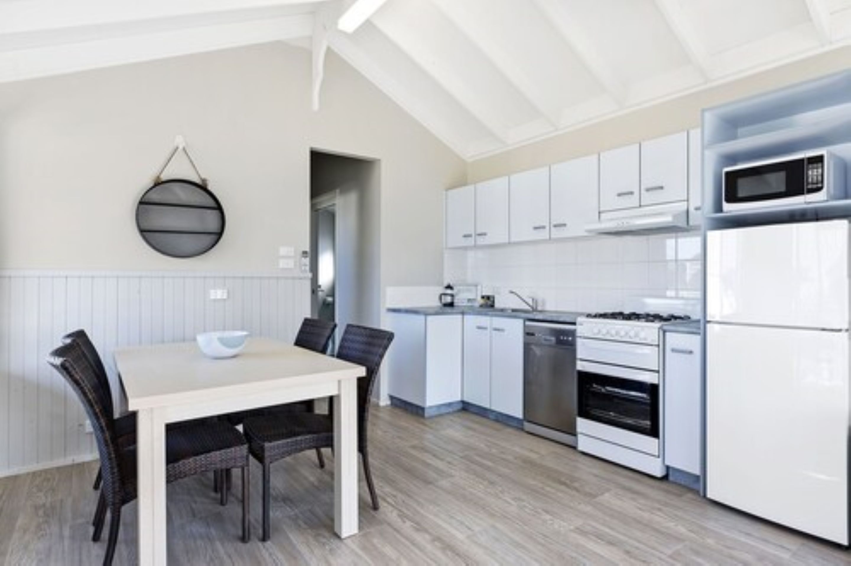 Une cuisine moderne avec des armoires blanches, un four à micro-ondes, une cuisinière et un lave-vaisselle. On y trouve une table à manger avec des chaises et un luminaire suspendu.