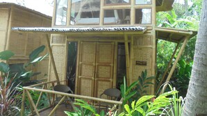 Estructura de bambú de dos pisos con balcón, rodeada de exuberante vegetación.