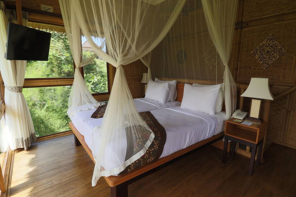A bed with a canopy, a bedside table with a lamp, and a TV mounted on the wall.