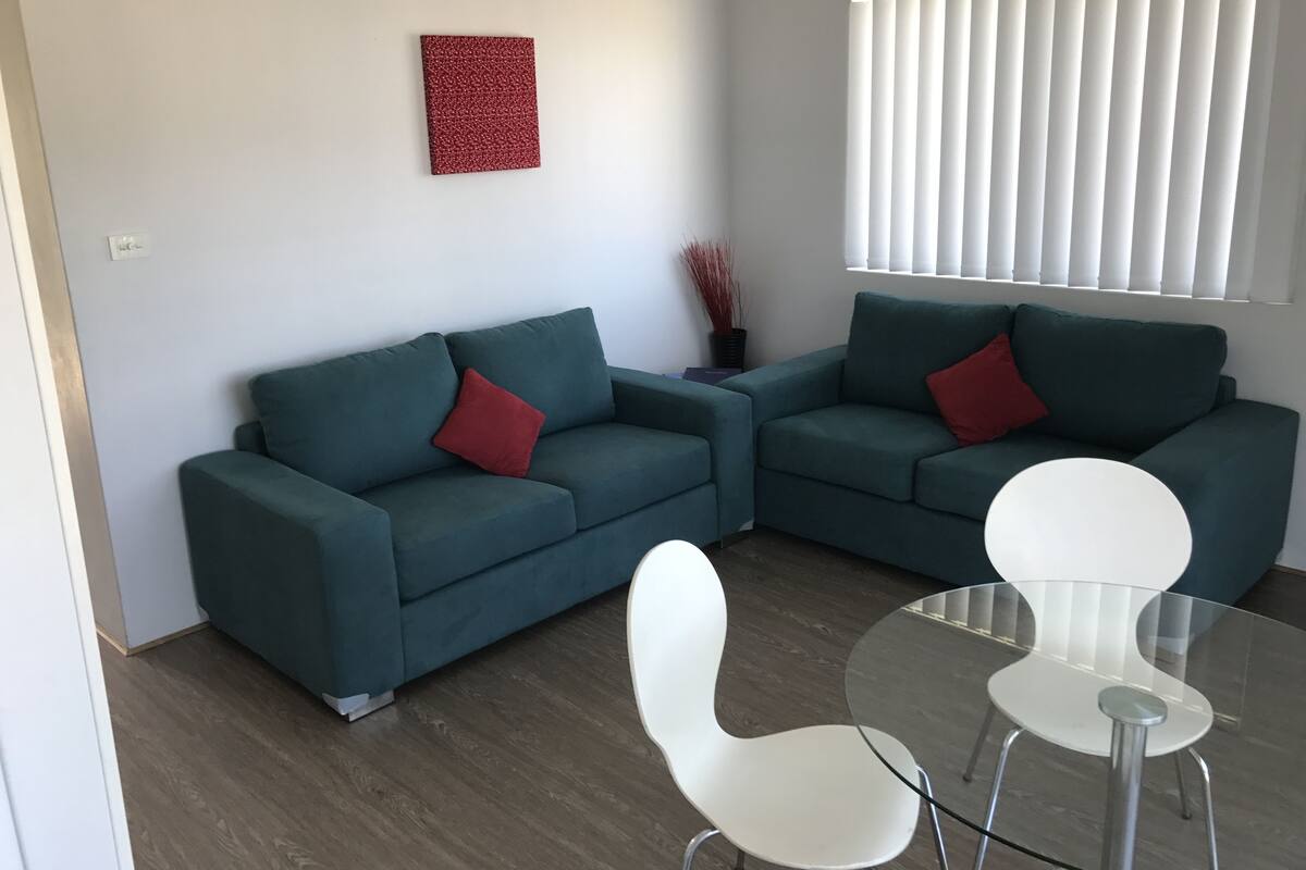 A modern living room with a sectional sofa, a glass coffee table, and white chairs.