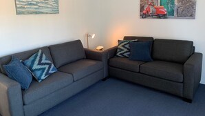 Una sala de estar con dos sofás grises, un tapete azul, una lámpara y dos cuadros.