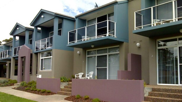 Un edificio residencial moderno de varios pisos, con balcones, techo plano y césped cuidado.