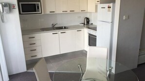 Una cocina moderna con armarios blancos, un microondas, un refrigerador, un hervidor y una mesa de vidrio.